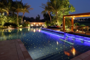 A creative cluster of fiber optic illuminations in the pool together with spike lights on the pergola and fire pots gives this garden an impression of a starry Arabian night in the desert.